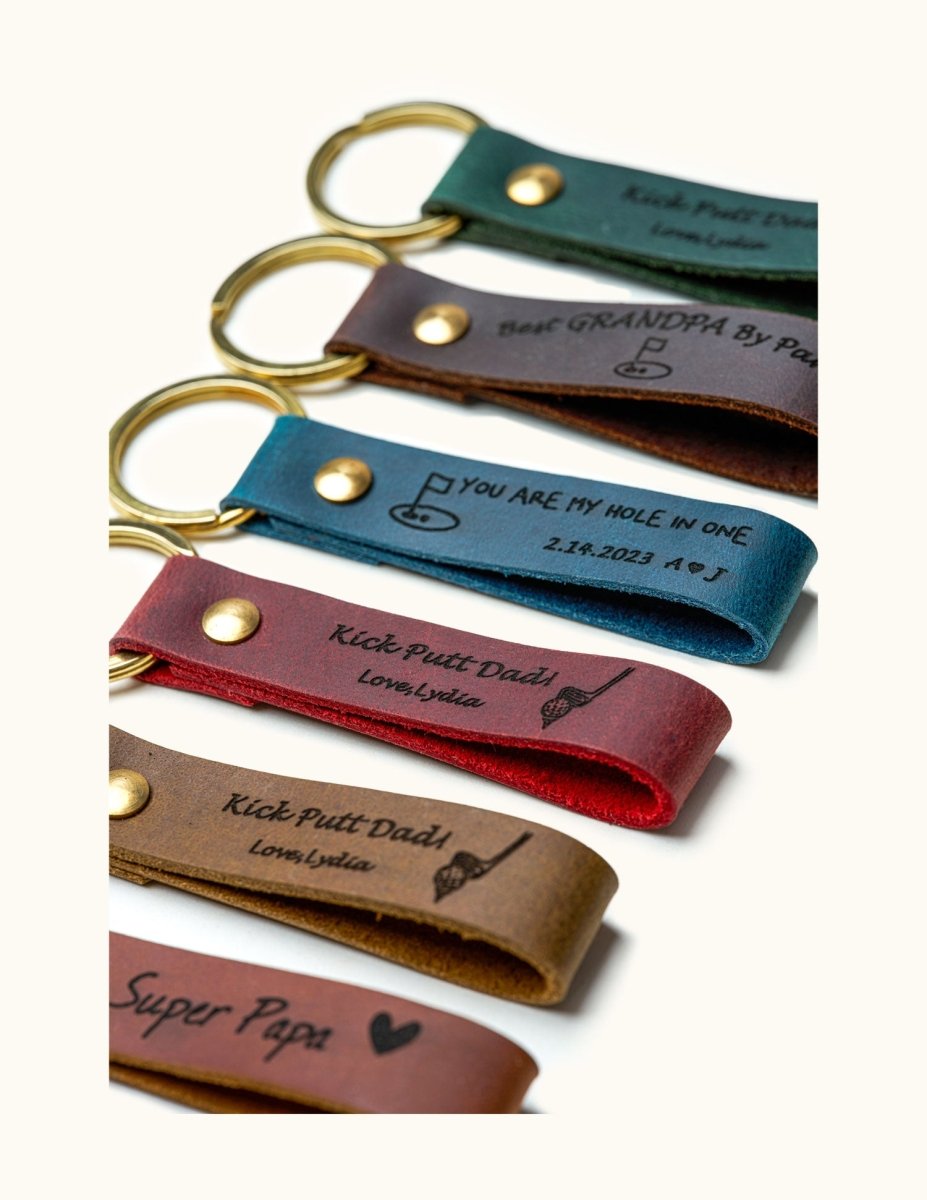 Close-up of handmade leather keychains with gold rings, engraved with golf-themed messages like “Kick Putt Dad” and “You Are My Hole In One,” perfect personalized gifts for golf dads, grandpas, and golf lovers.