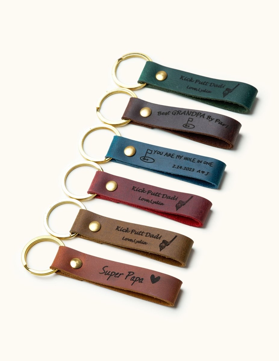 Angled view of handmade leather keychains with gold rings, engraved with golf-themed messages like “Kick Putt Dad,” “Best Grandpa By Par,” and “You Are My Hole In One,” ideal personalized gifts for golf dads and grandpas.