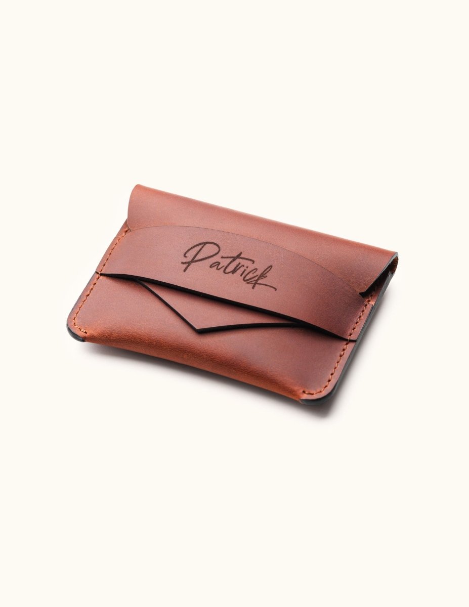 Handcrafted brown leather wallet with personalized name engraving, shown in angled view highlighting the slim minimalist card holder and envelope flap design.