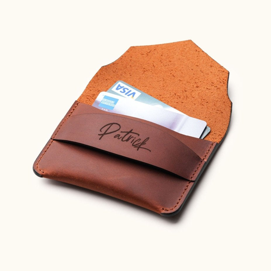 Open view of handcrafted brown leather wallet with personalized name engraving, showing credit cards inside minimalist slim card holder with envelope flap.