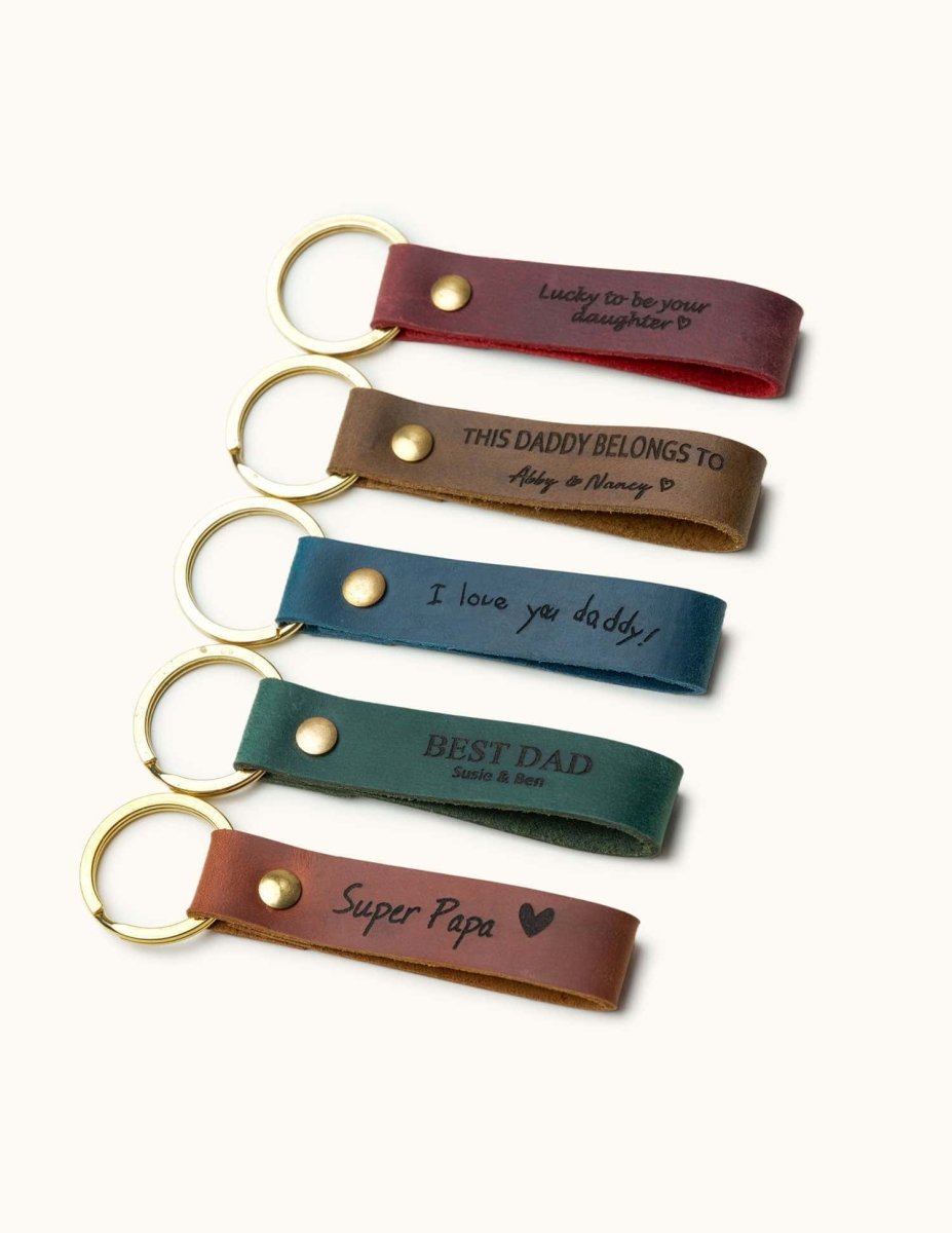 Five handcrafted leather keychains in red, brown, blue, green, and tan with gold rings, engraved with messages like “Super Papa” and “Best Dad,” perfect Father’s Day or birthday gifts for dad.