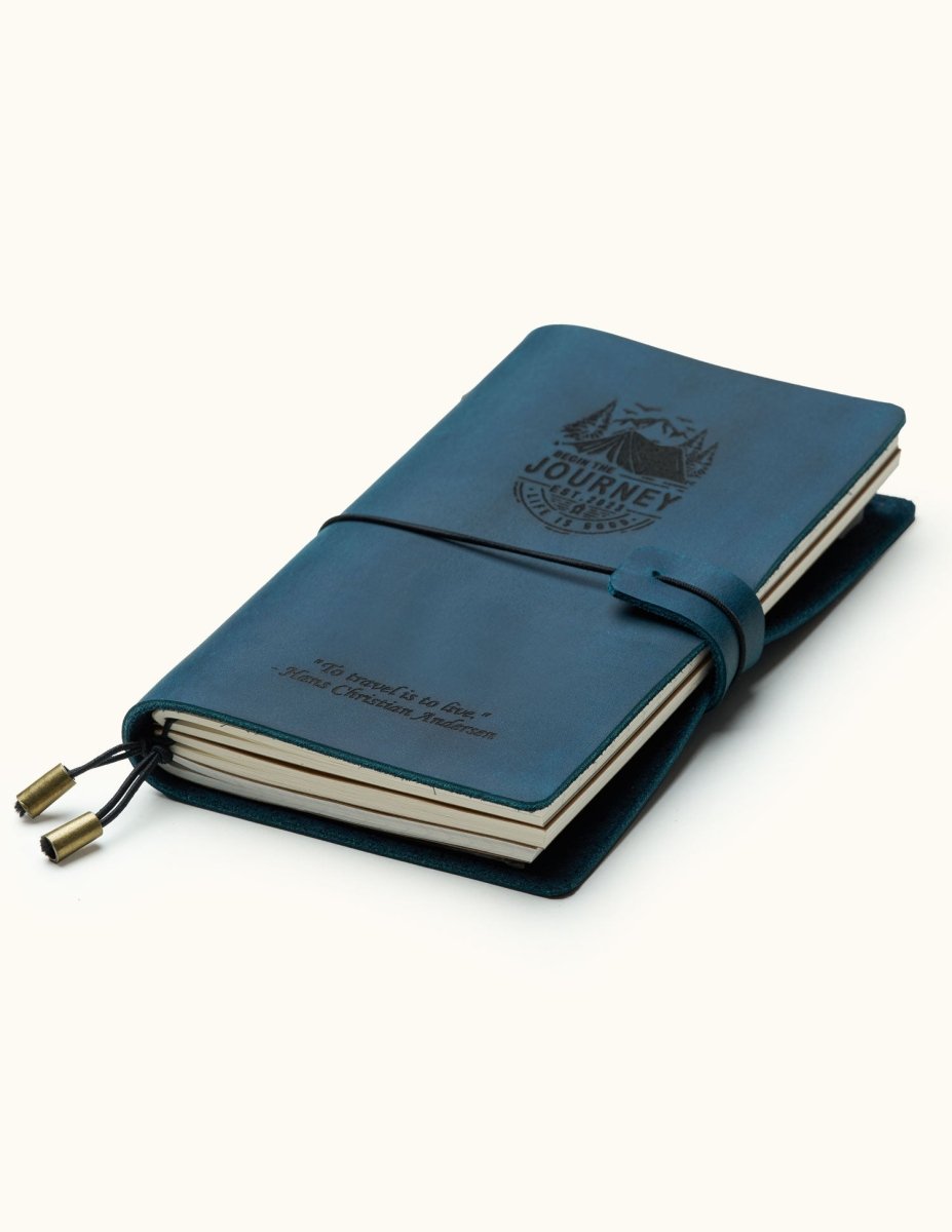 Handcrafted navy blue leather travel journal with elastic closure, custom engraved mountain adventure design, refillable pages, and brass charms, perfect for travel notes and journaling.