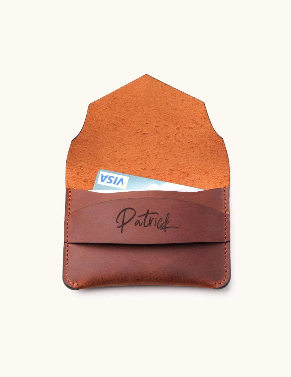 Handcrafted brown leather wallet shown open with visible suede interior, holding a credit card in the personalized slim card holder with name engraving and envelope flap design.