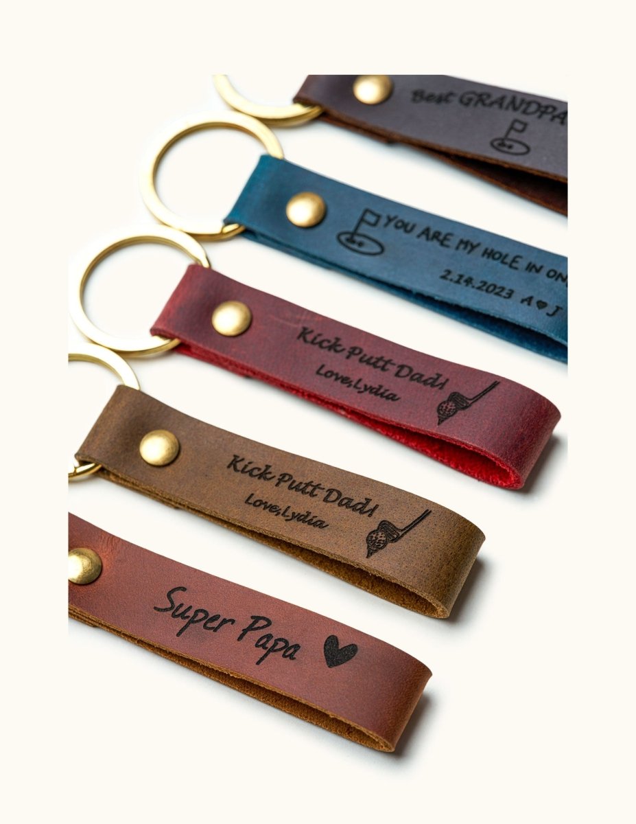 Close-up of personalized leather keychains with gold rings, engraved with golf-themed messages like “Kick Putt Dad” and “You Are My Hole In One,” ideal custom gifts for dads, grandpas, and golfers.
