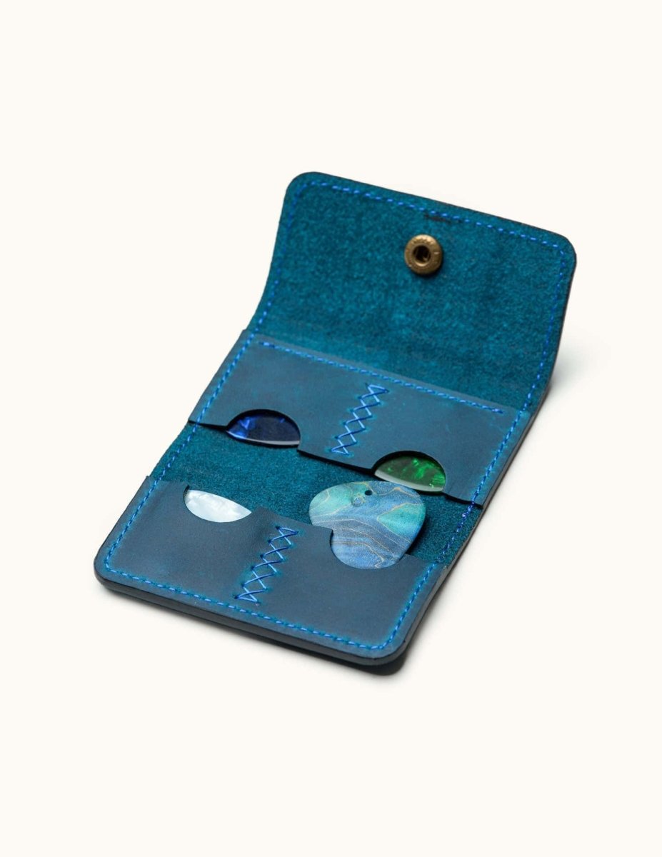 Open view of blue leather guitar pick holder with colorful picks and hand-stitched details, showcasing six organized slots
