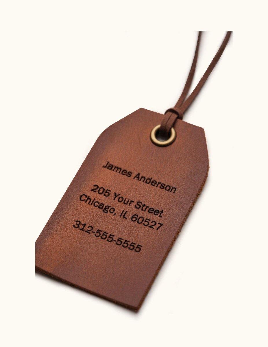 Close-up of a vintage brown leather luggage tag with engraved contact information, brass eyelet, and leather tie detail