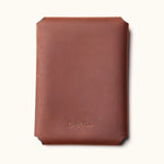 Back view of a brown full-grain leather Kindle sleeve embossed with the CraftedMan logo, showcasing the clean stitching-free design