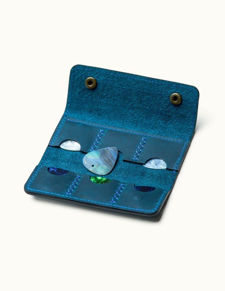 Open custom blue leather guitar pick case with six slots and colorful picks, featuring central marbled pick and double snap buttons