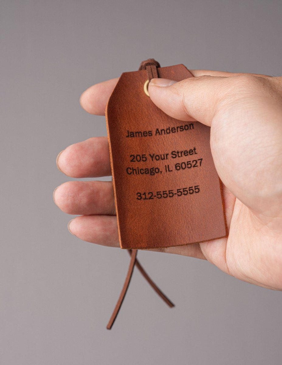 Hand holding a personalized vintage brown leather luggage tag with engraved name, address, and phone number