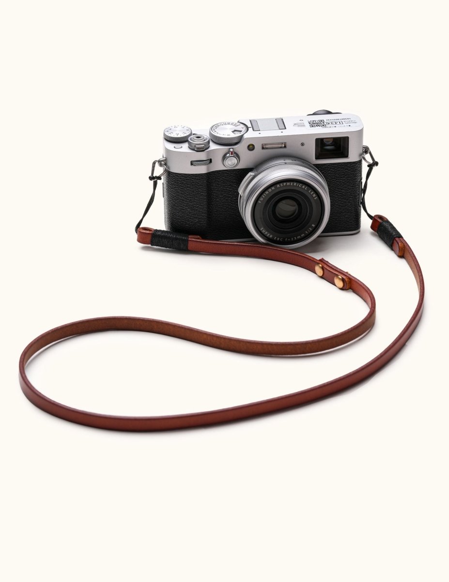 Handmade full-grain leather camera strap attached to Fujifilm vintage-style mirrorless camera, shown laid out on white background