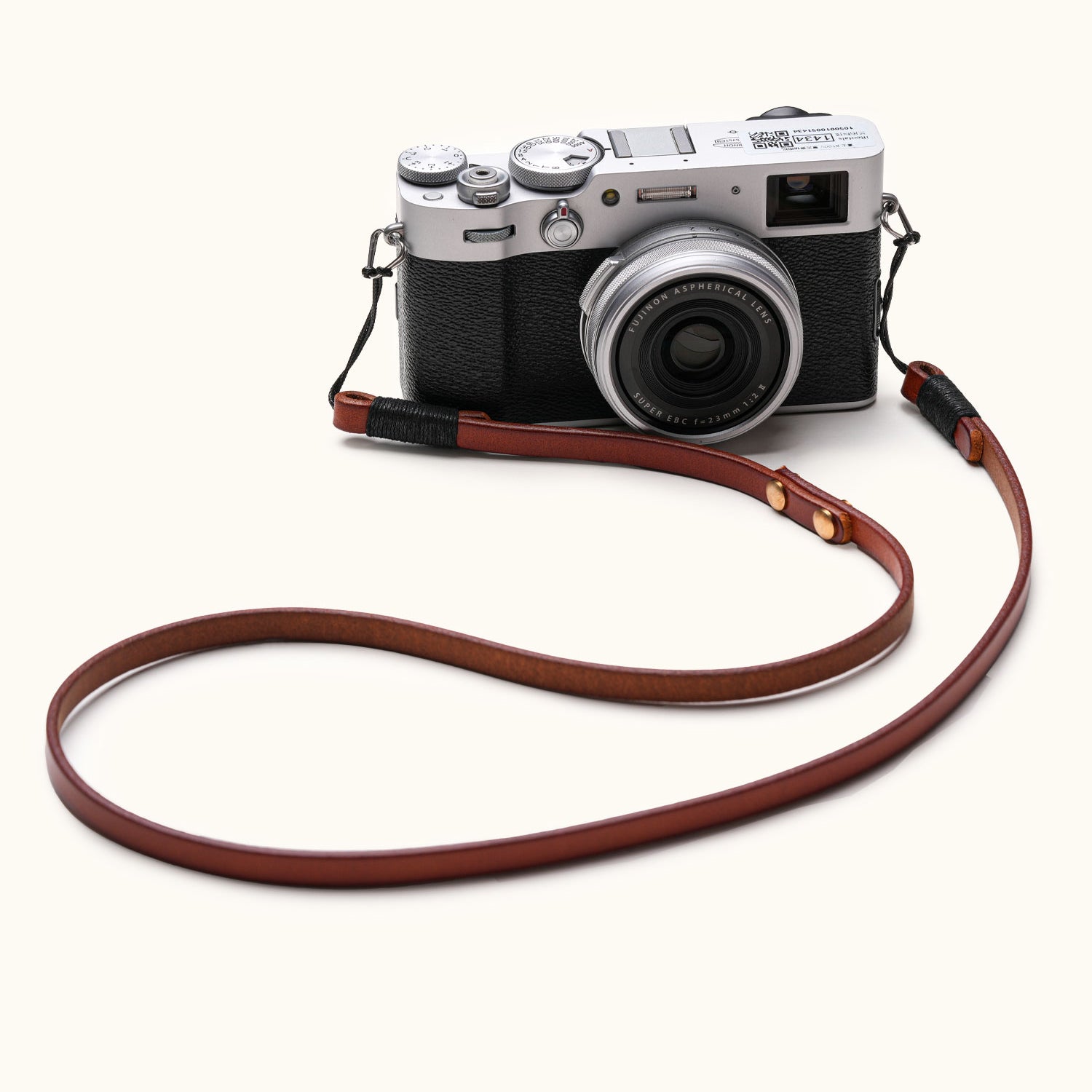 Handmade full-grain leather camera strap attached to Fujifilm vintage-style mirrorless camera, shown laid out on white background
