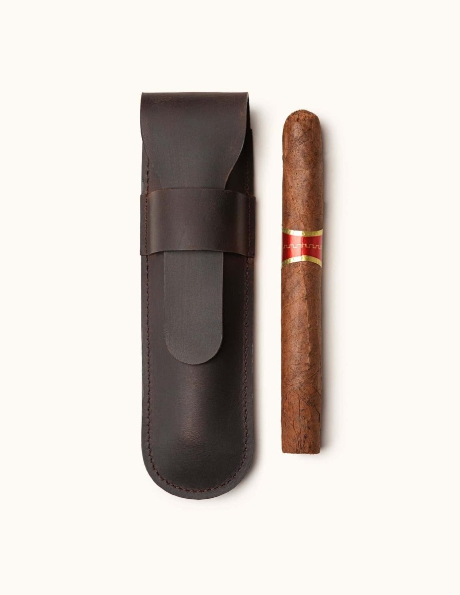 Handmade dark brown leather cigar pouch designed for one cigar, shown with a full-sized cigar beside it. A minimalist, travel-friendly accessory for cigar lovers