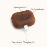 Bottom view of a personalized leather AirPods case plugged into a white charging cable. Demonstrates easy access to the charging port without removing the cover.