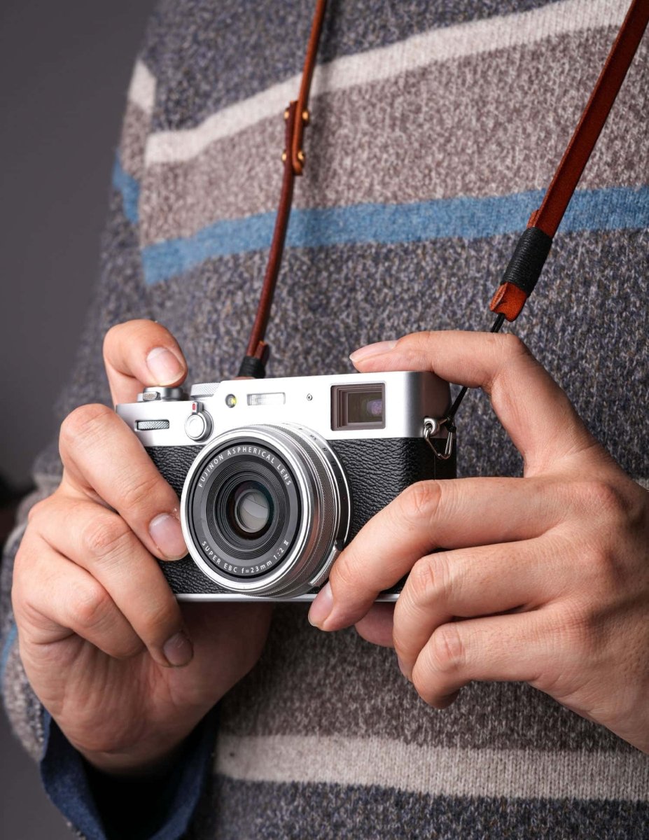 Handmade leather camera strap worn around neck with Fujifilm mirrorless camera in hand, showing natural fit and style