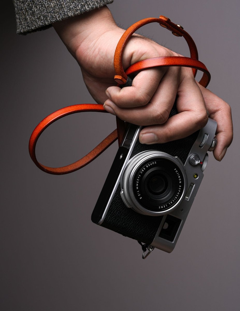 Handcrafted leather camera strap wrapped around hand holding a Fujifilm vintage-style mirrorless camera