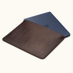 Coffee brown leather laptop sleeve with a dark blue laptop partially inserted, showing the open top and stitched edges.