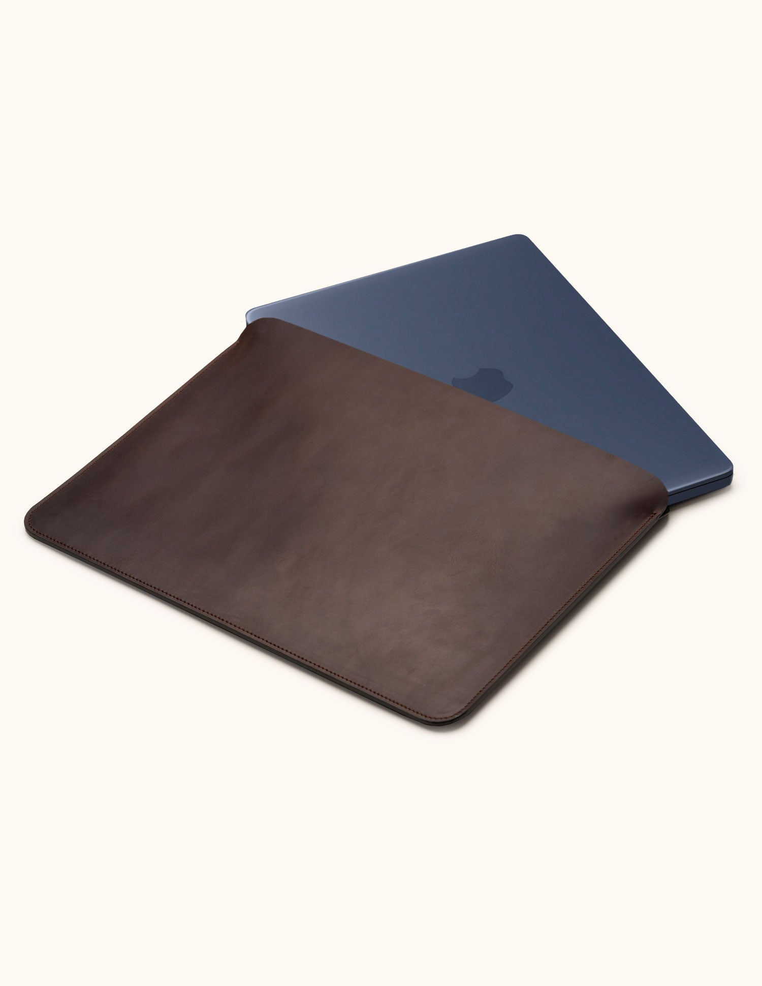 Coffee brown leather laptop sleeve with a dark blue laptop partially inserted, showing the open top and stitched edges.