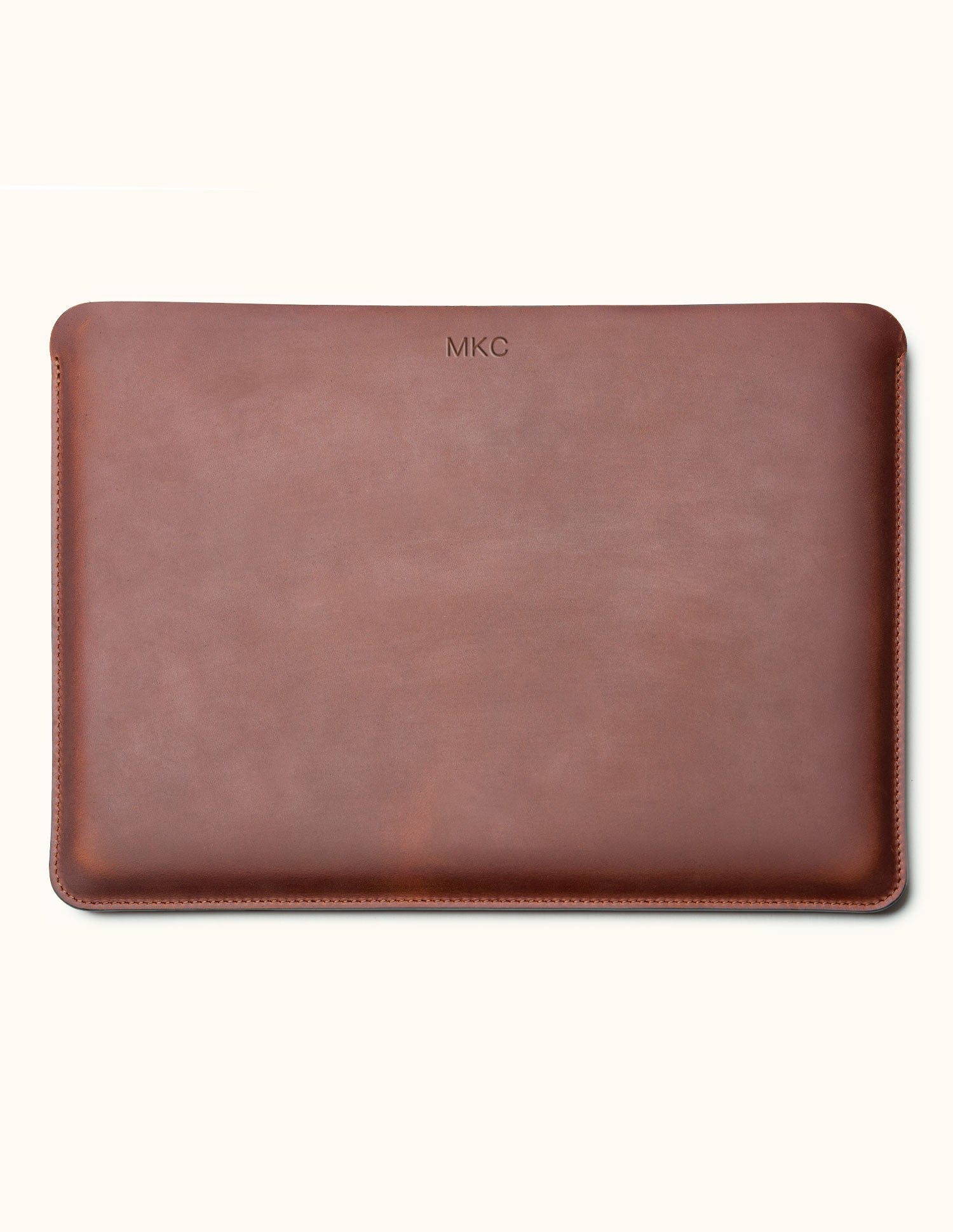 Front view of a vintage brown leather laptop sleeve with a small monogram near the top center and stitched edges.