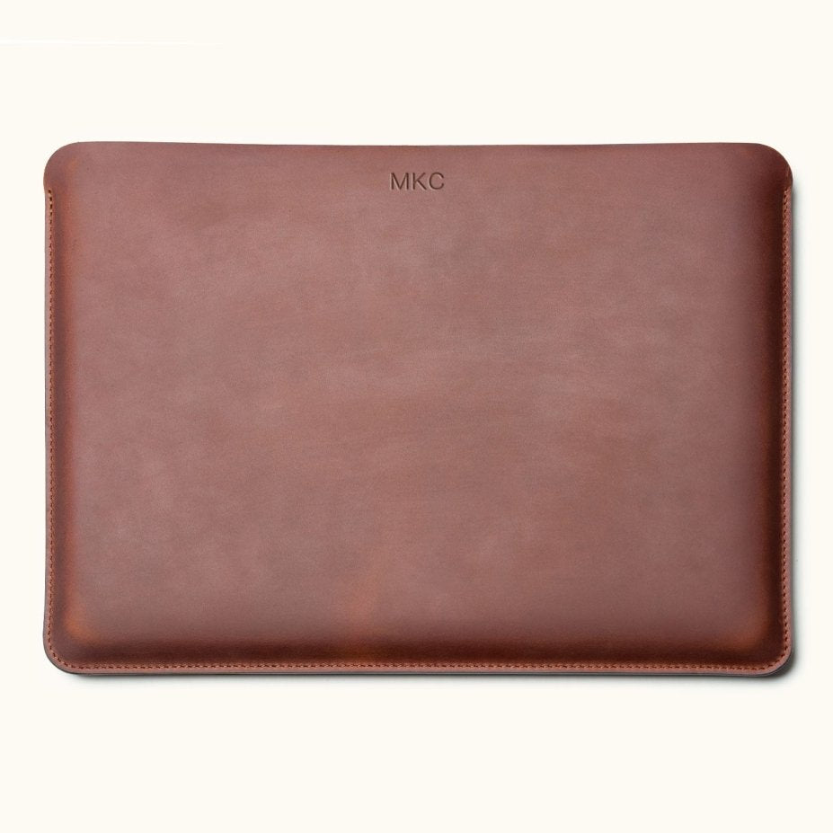 Front view of a vintage brown leather laptop sleeve with a small monogram near the top center and stitched edges.