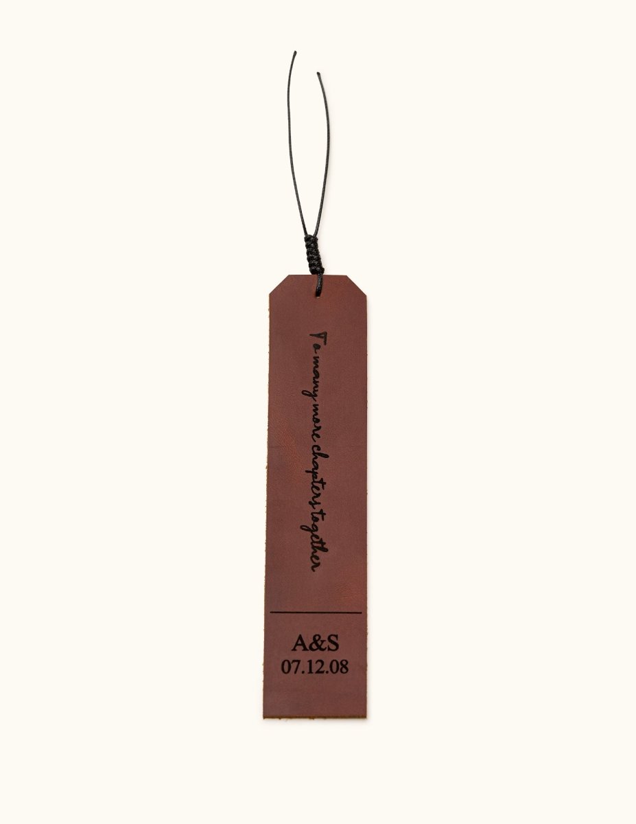 Brown leather bookmark engraved with "To many more chapters together" and personalized initials and date "A&S 07.12.08", shown on a plain background