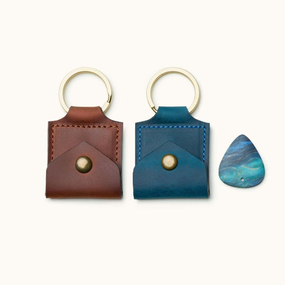 Two square leather guitar pick holder keychains in brown and blue, shown with a pick for size reference