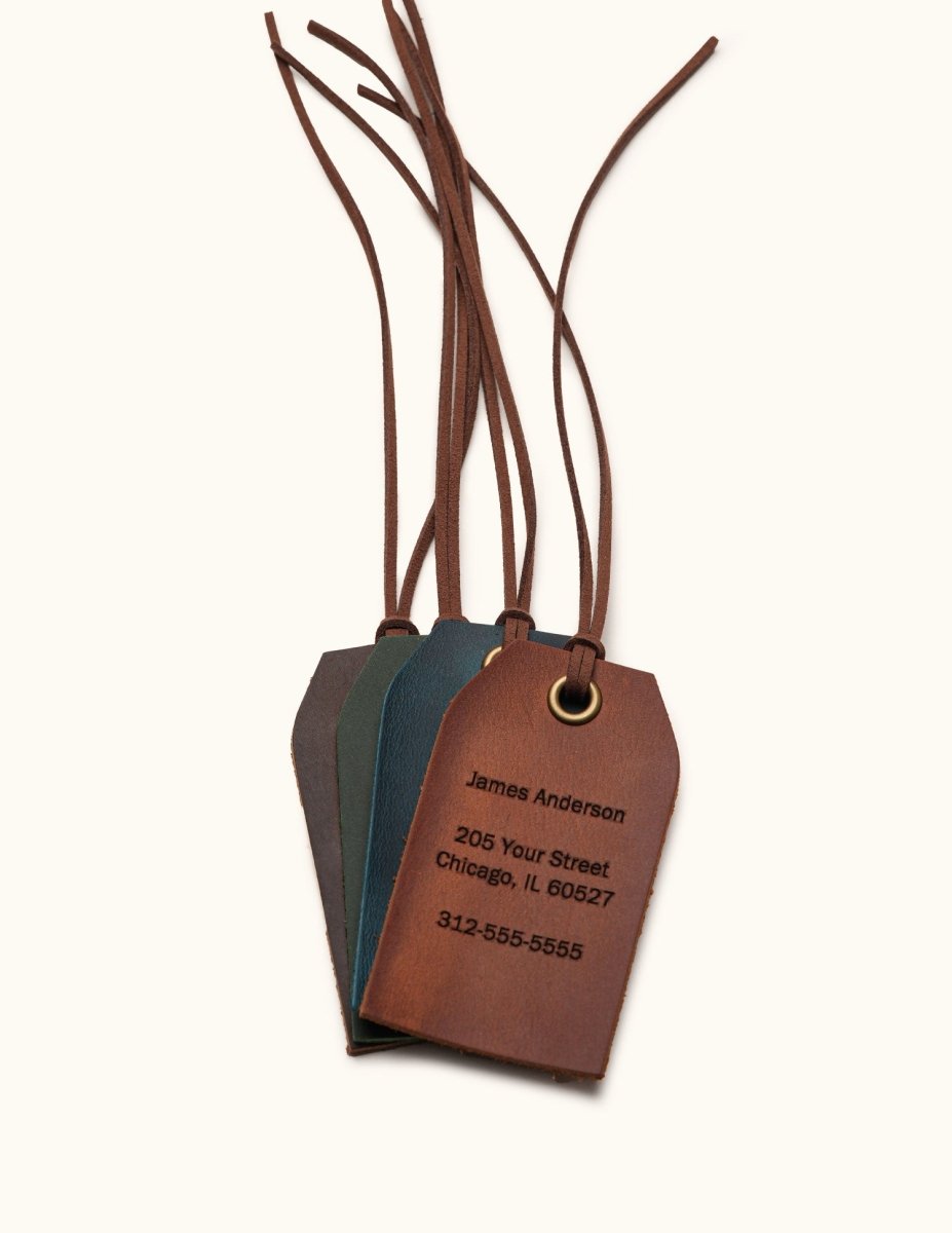 Stack of four personalized leather luggage tags in Coffee, Green, Navy, and Vintage Brown, featuring engraved contact information and leather straps