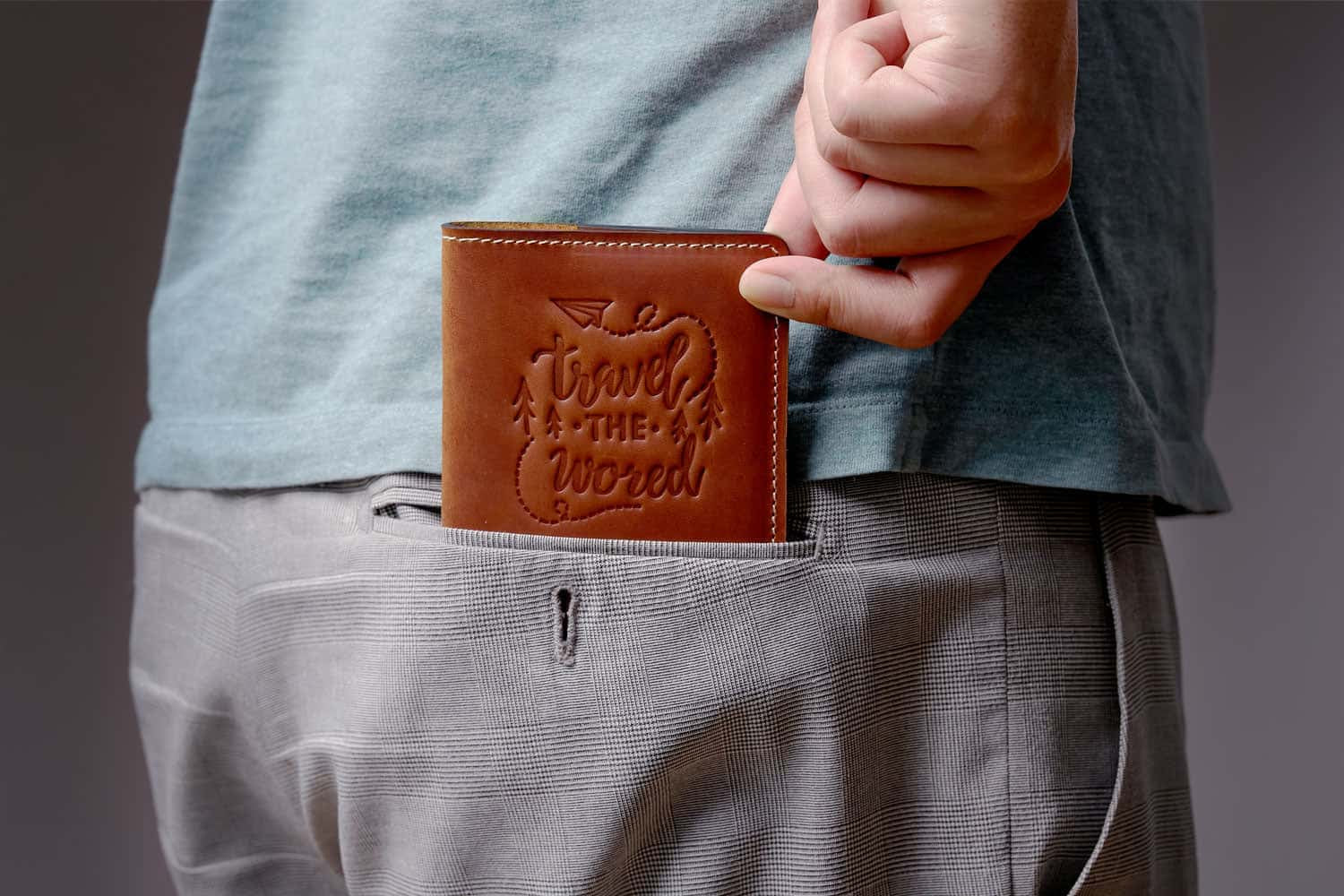 Man holding a vintage brown leather passport cover with 'Travel the World' design, easily fitting into a back pocket – ideal for minimalist travelers