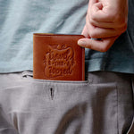 Man holding a vintage brown leather passport cover with 'Travel the World' design, easily fitting into a back pocket – ideal for minimalist travelers