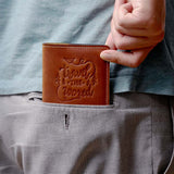 Man holding a vintage brown leather passport cover with 'Travel the World' design, easily fitting into a back pocket – ideal for minimalist travelers