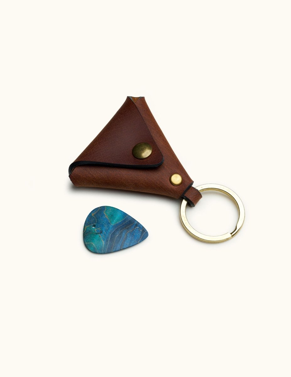 Triangular leather guitar pick holder with keyring and brass snap, shown with a blue pick