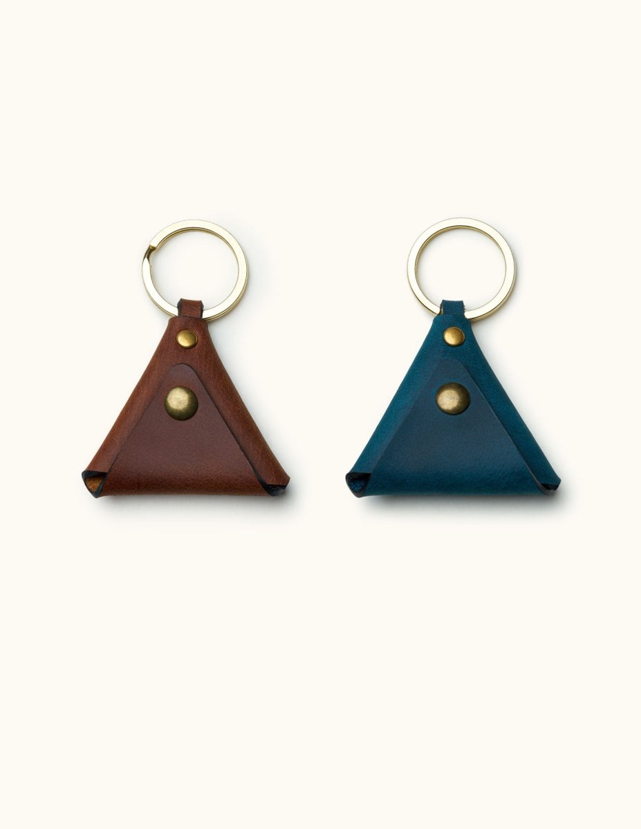 Two triangular leather guitar pick holders with keyrings in brown and blue color options, featuring brass snap buttons